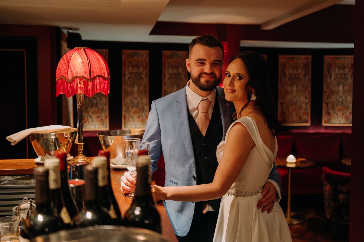 A couple shares an intimate moment in a dimly lit room with vintage decor and red lamp.