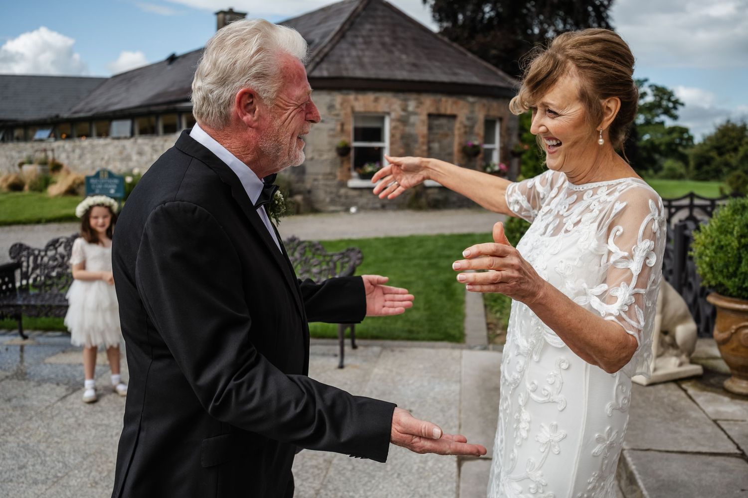 Two people in formal attire sharing an animated conversation outside a rustic stone building.