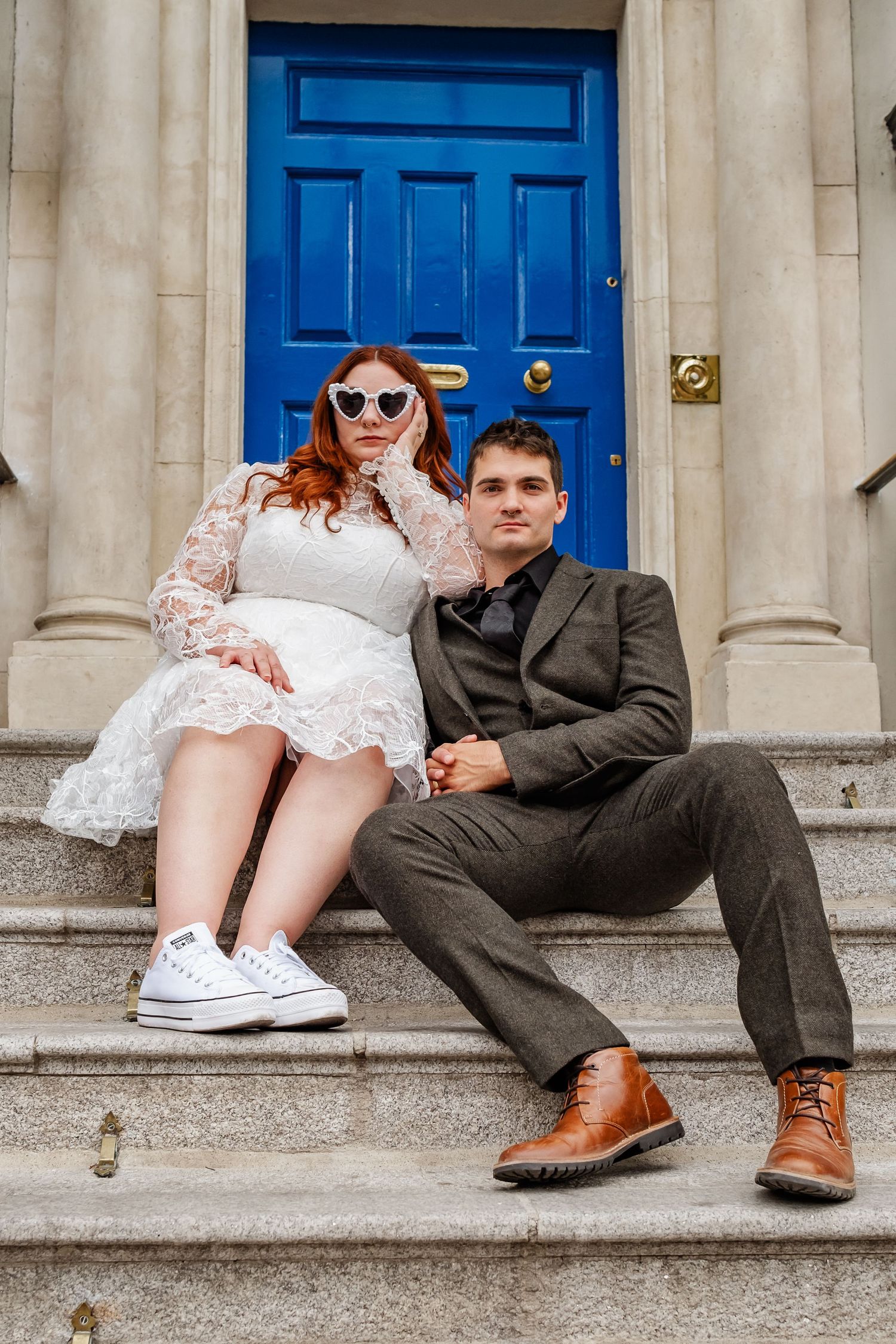 Couple sitting on stone steps in front of bright blue door wearing formal and casual attire.