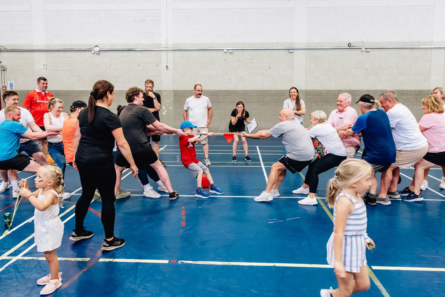 Large group playing tug of war on indoor blue court with spectators watching.