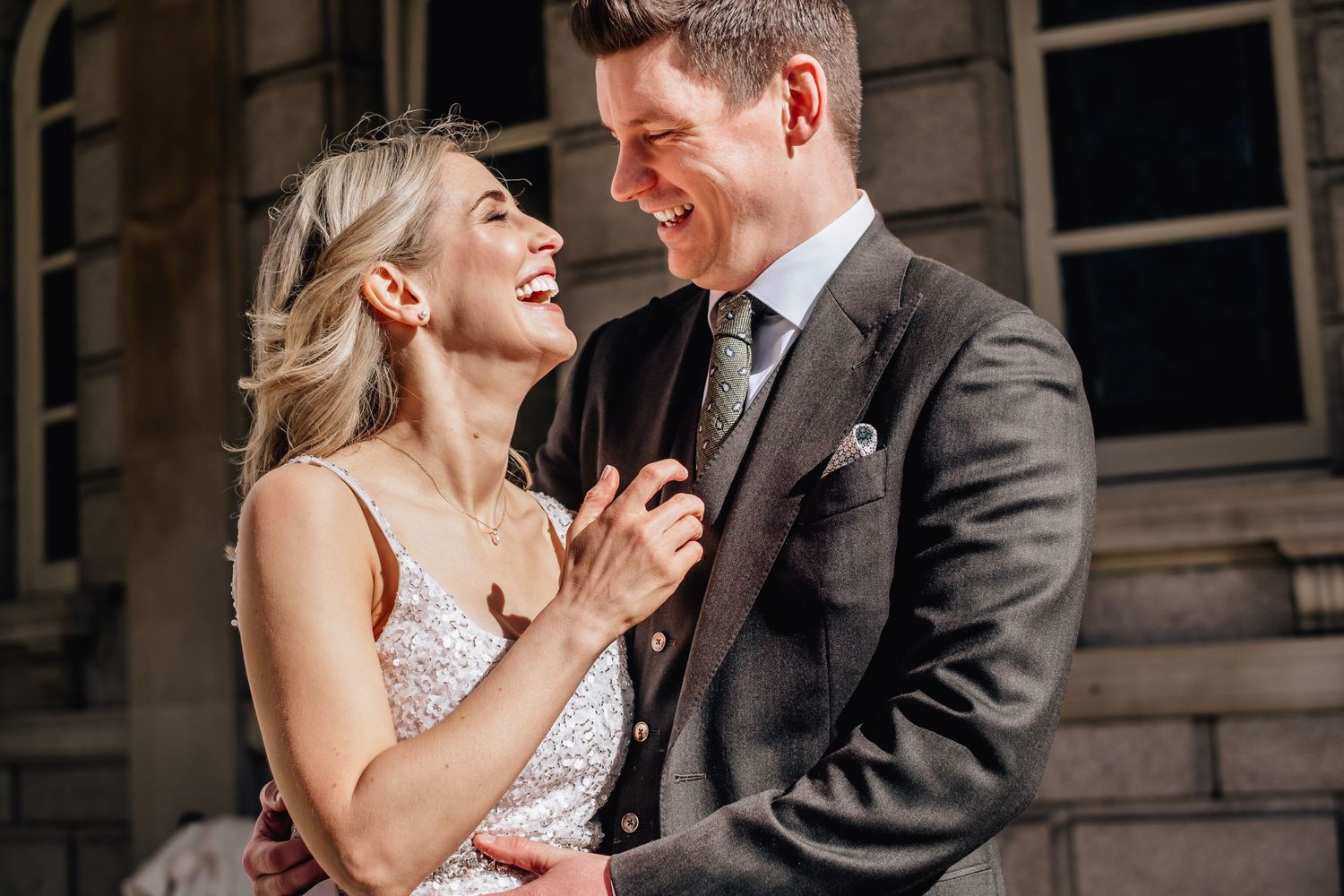 Candid moment of joyful laughter between couple in formal attire against rustic backdrop.