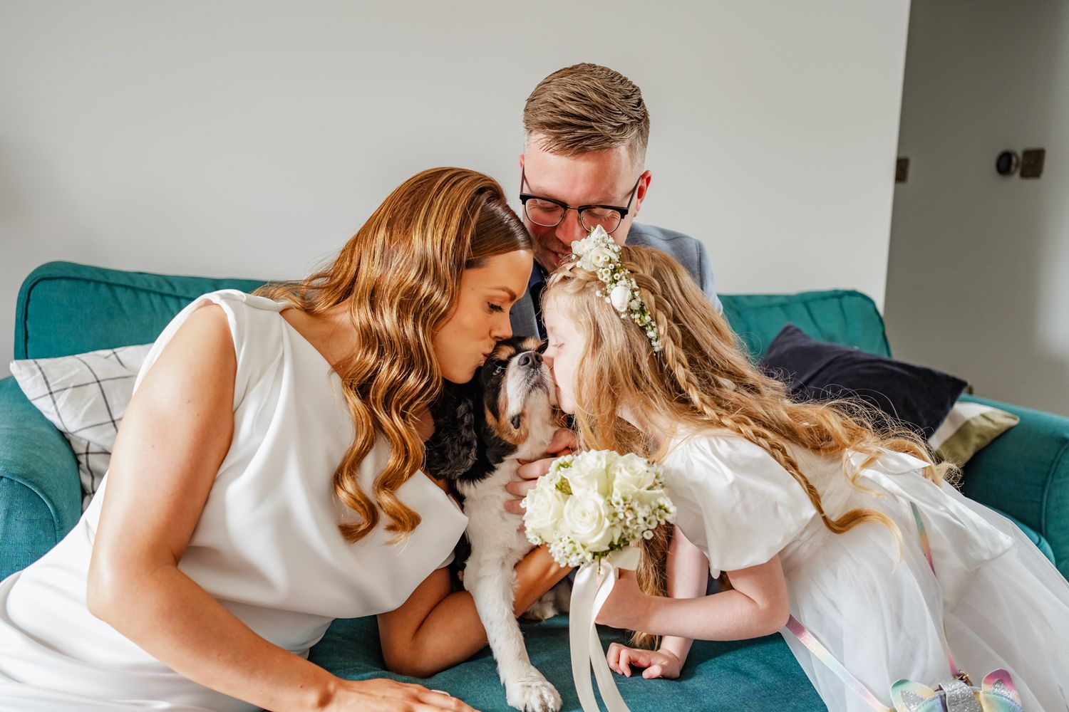 Intimate family moment on teal couch with white flowers and formal attire.