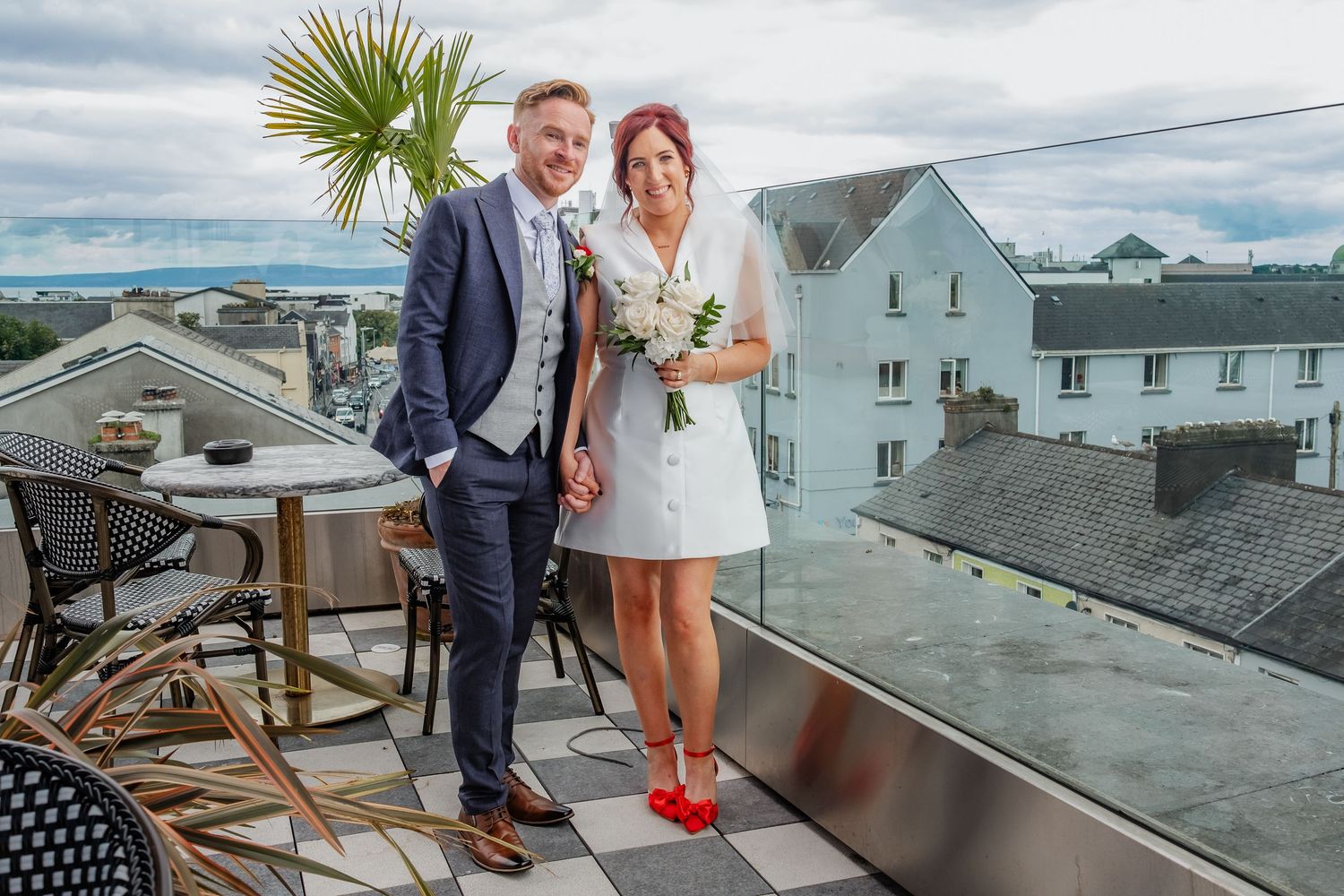 Couple posing for wedding photos on a coastal rooftop with seaside buildings in the background.