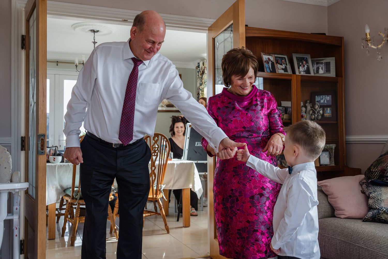 Grandfather dancing with young boy in suit while grandmother watches at family wedding.