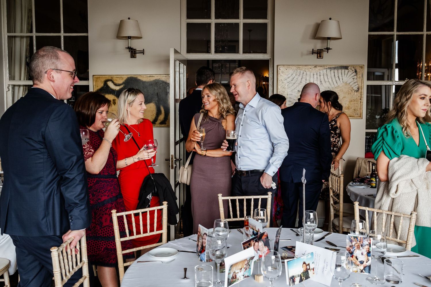 Elegantly dressed wedding guests socializing and holding drinks at a beautifully set reception dinner table.