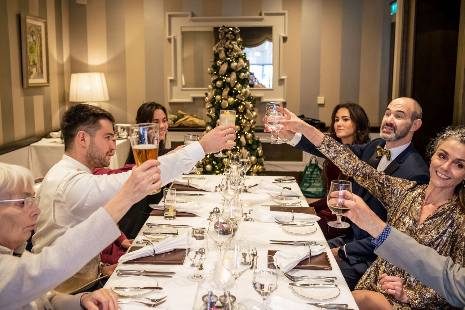 Family and friends toasting glasses at a festive Christmas dinner party around an elegantly set dining table.
