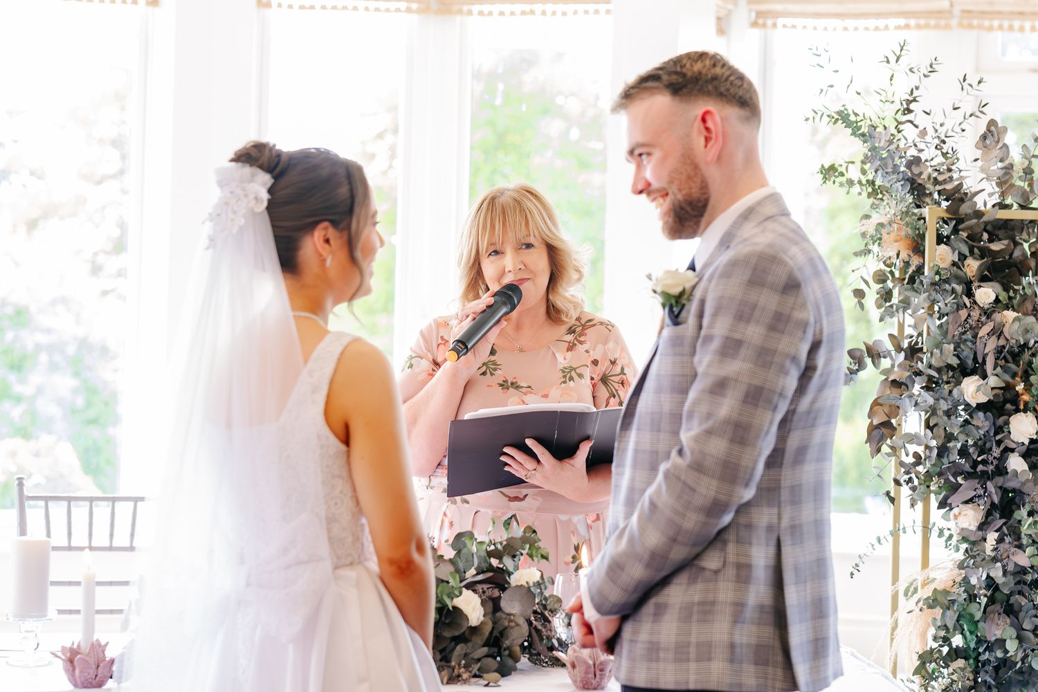 A bride and groom exchange vows with a female officiant during an elegant indoor wedding ceremony.