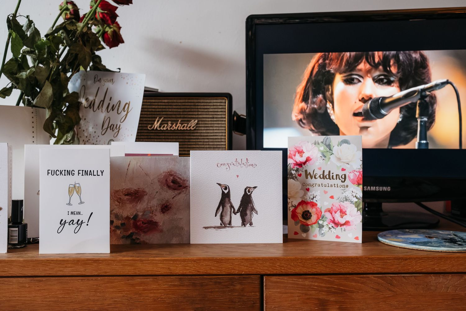 Collection of greeting cards and photos displayed on a wooden surface with a computer screen.