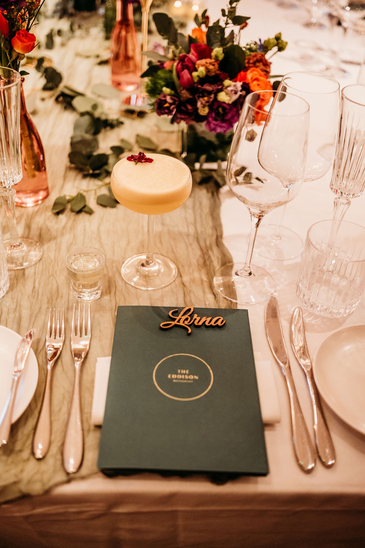 Two hands raise champagne glasses in a toast across an elegantly decorated wedding table.