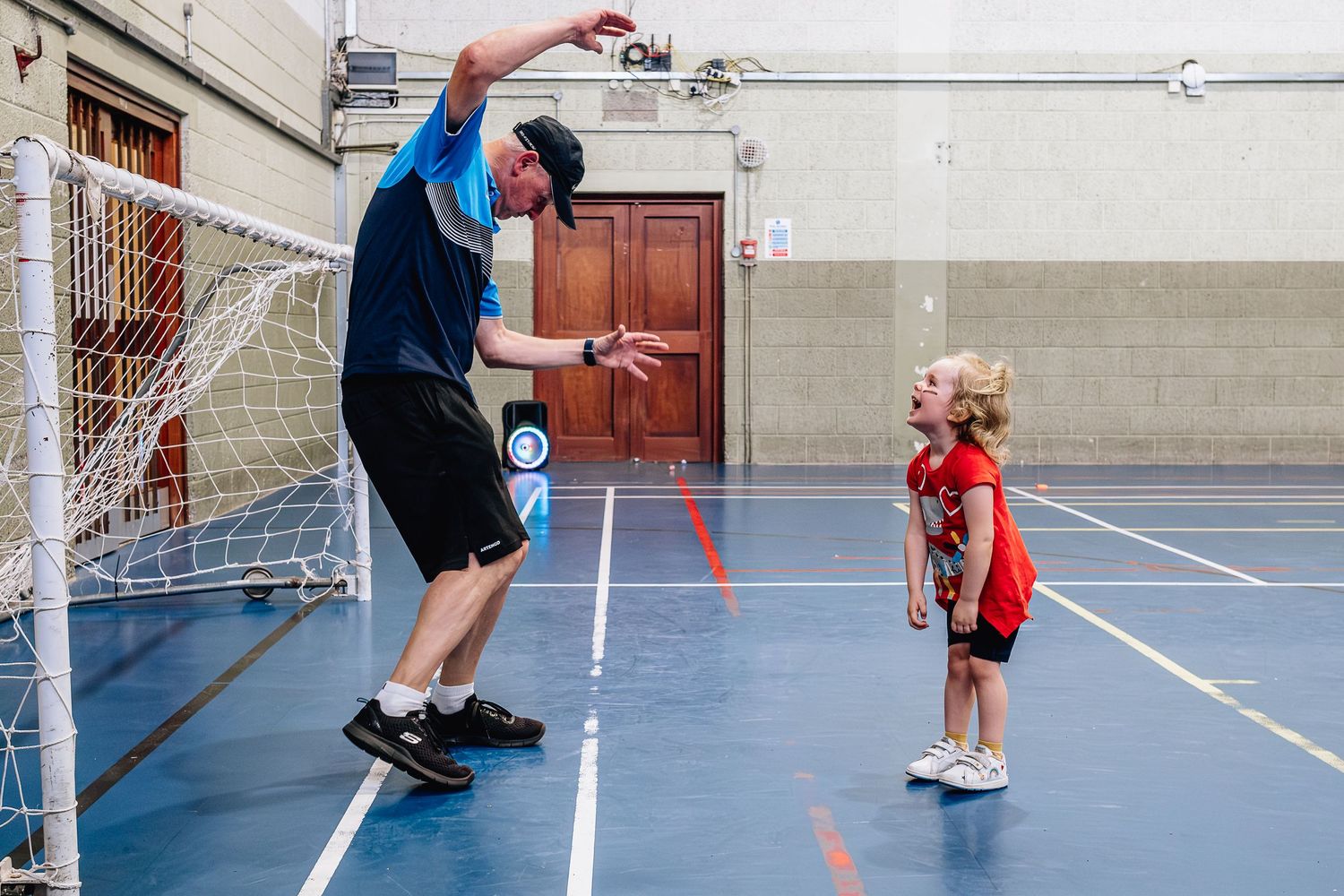 Adult demonstrating jumping exercise to child in indoor gymnasium.