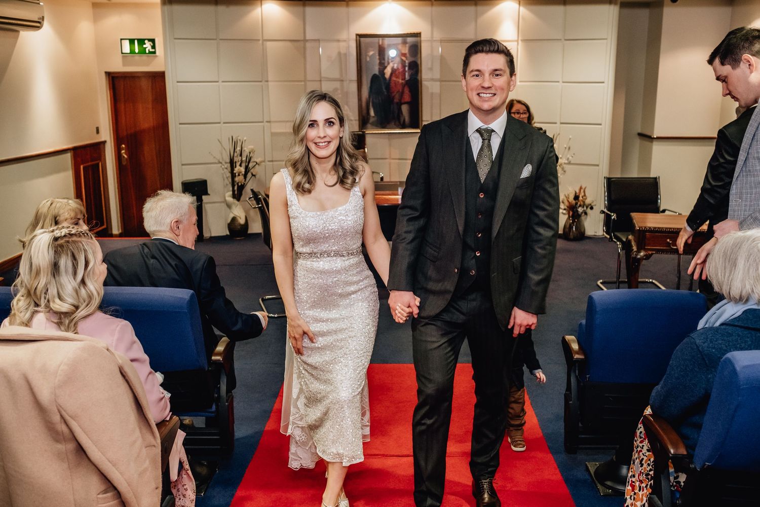 Wedding couple walks down red-carpeted aisle while guests look on in church venue.