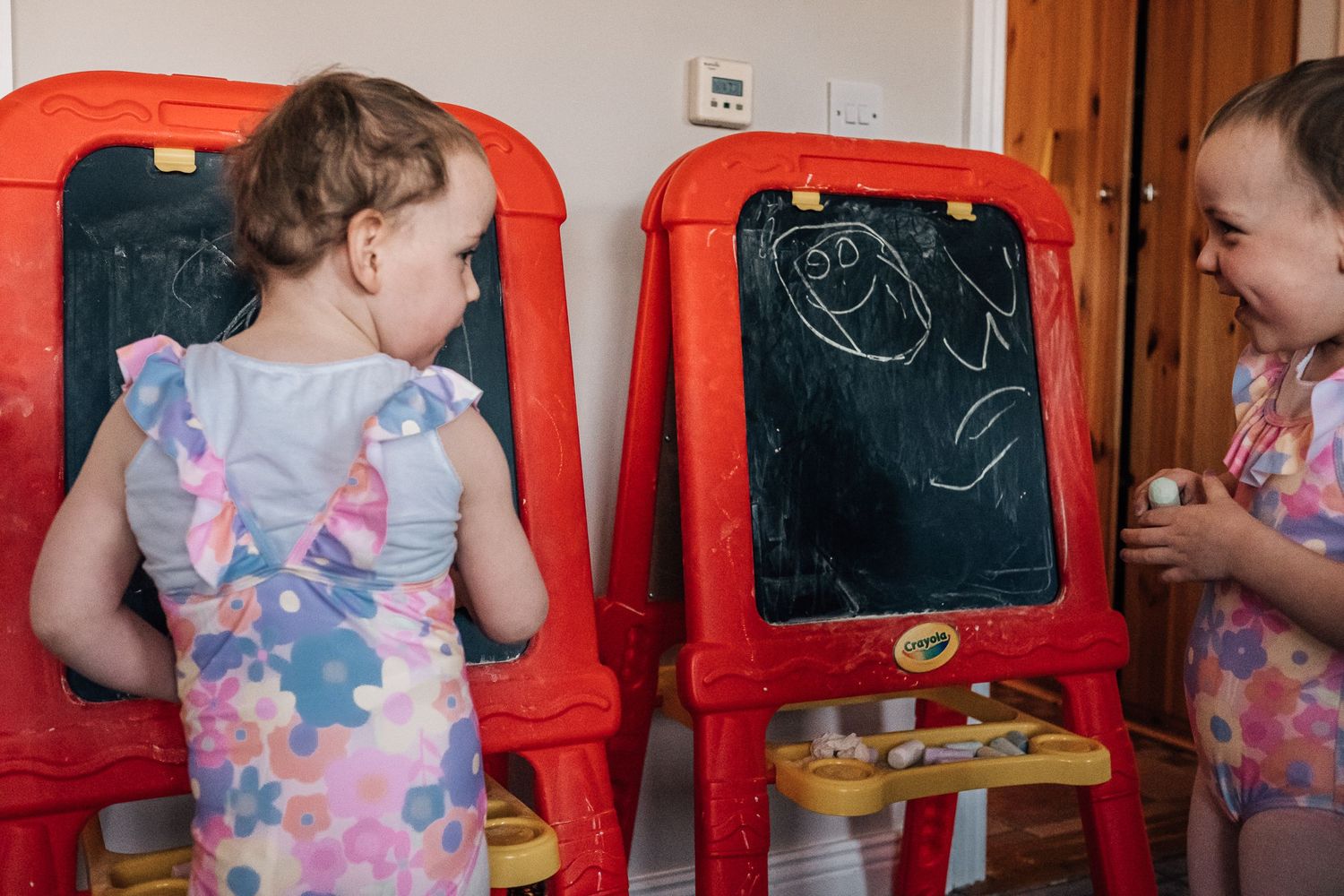 Two small children drawing on red plastic easels.