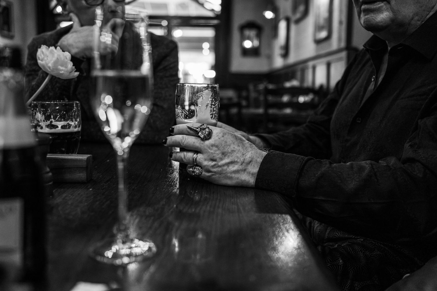 Black and white image of hands holding drinks at a bar counter.