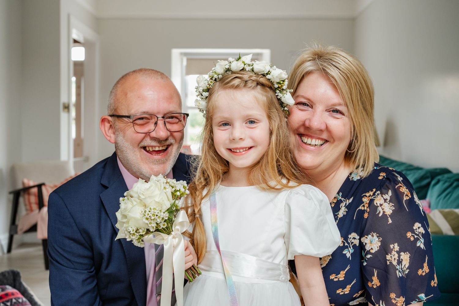 Family portrait with young flower girl in white dress holding bouquet.
