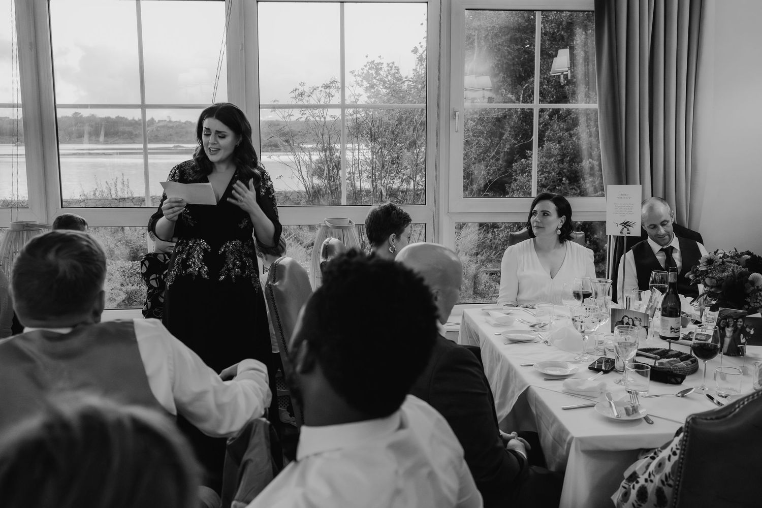 Woman giving a speech at an elegant wedding reception dinner in a black and white photo.
