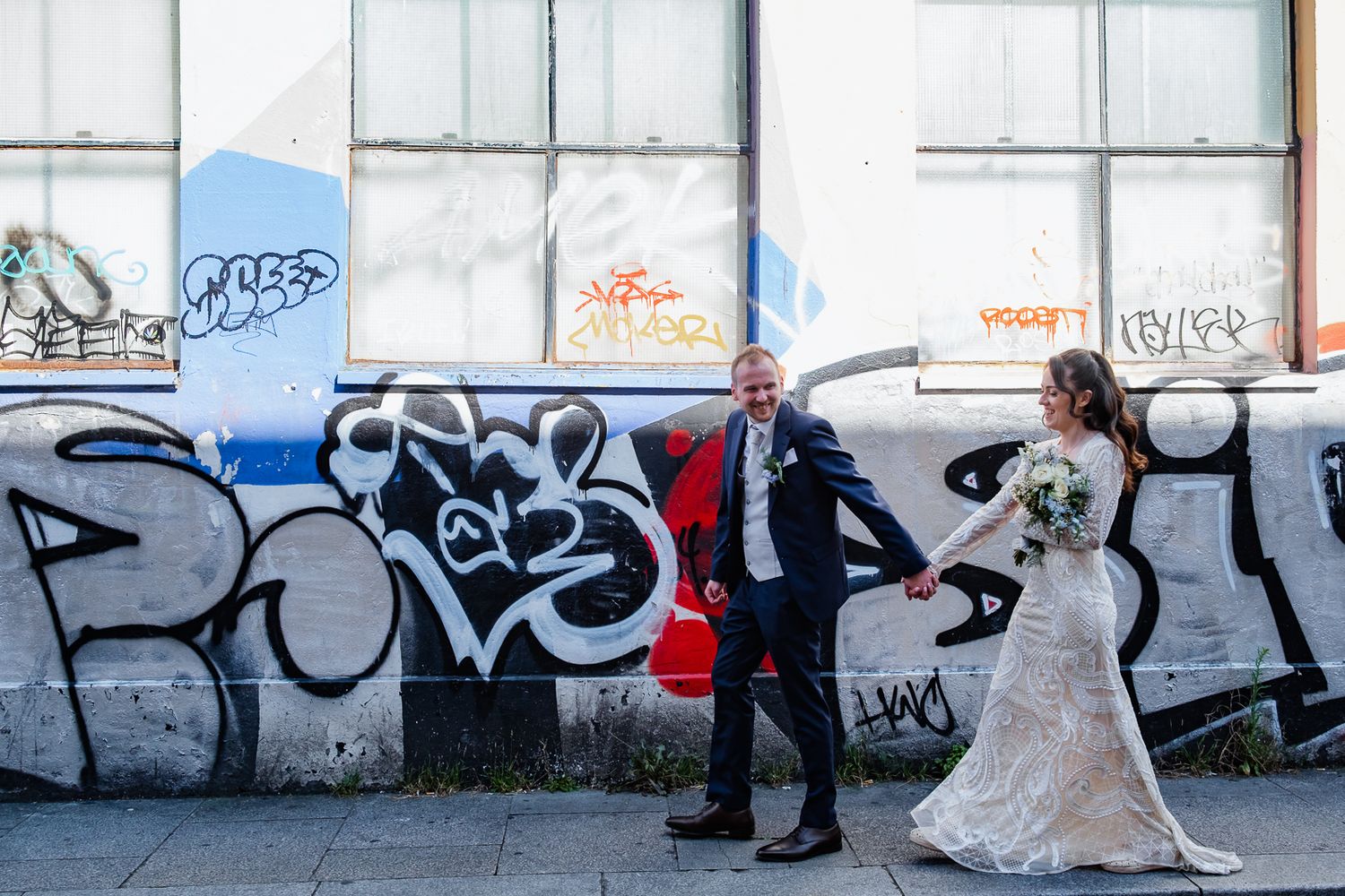 Wedding couple posing against urban graffiti wall.