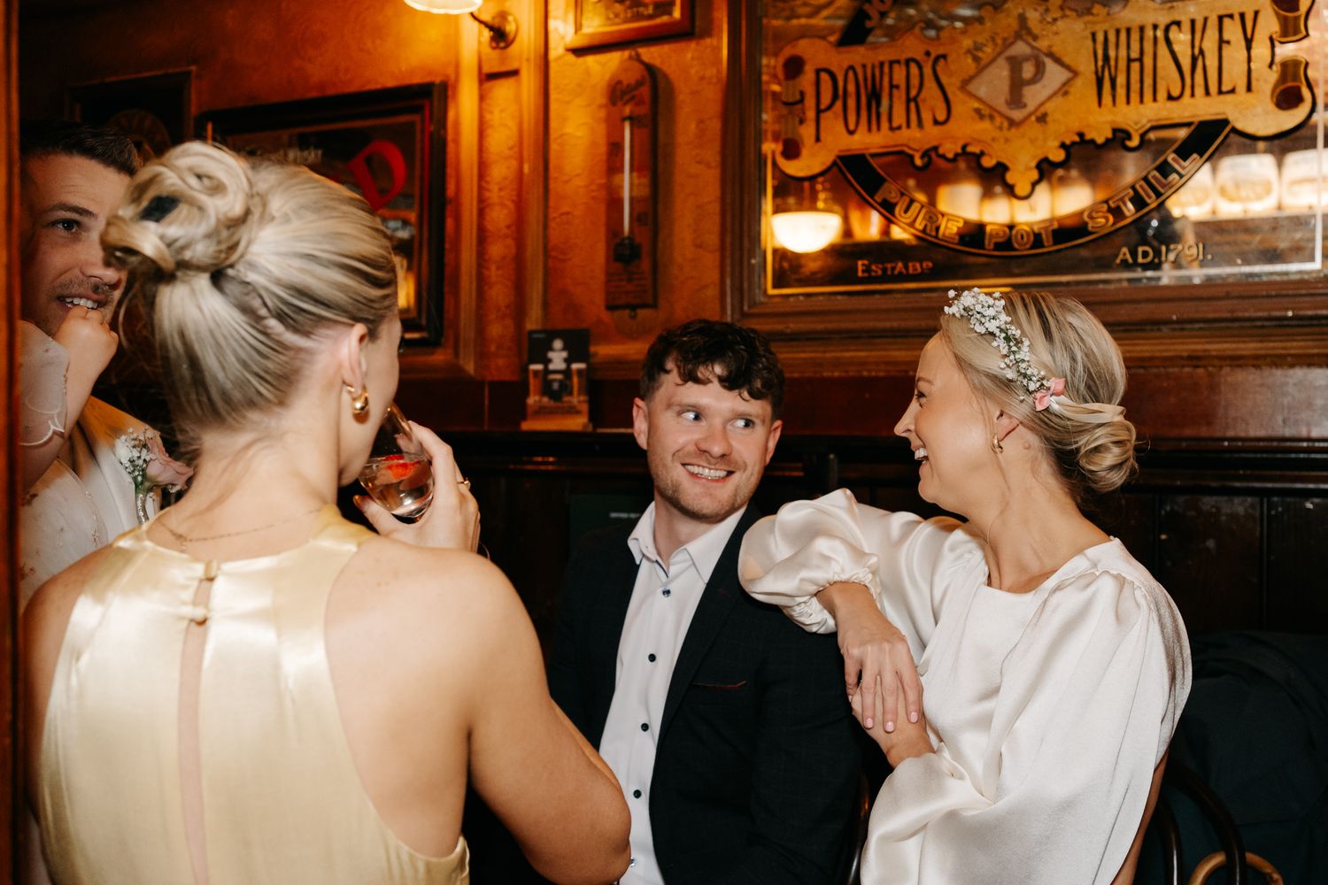 Guests socializing at a whiskey bar during a wedding reception in a warmly lit pub setting.