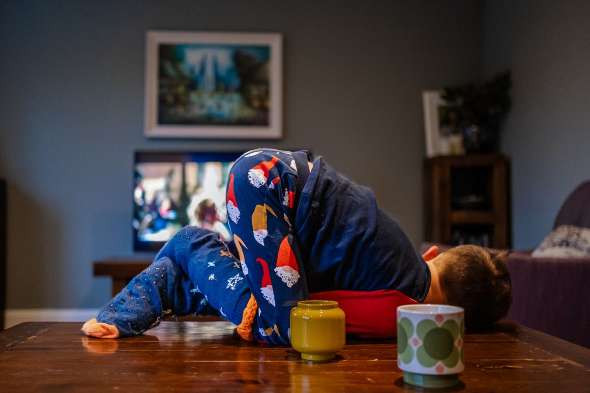 Two children in pajamas resting their heads on a wooden table while watching TV in a cozy living room.