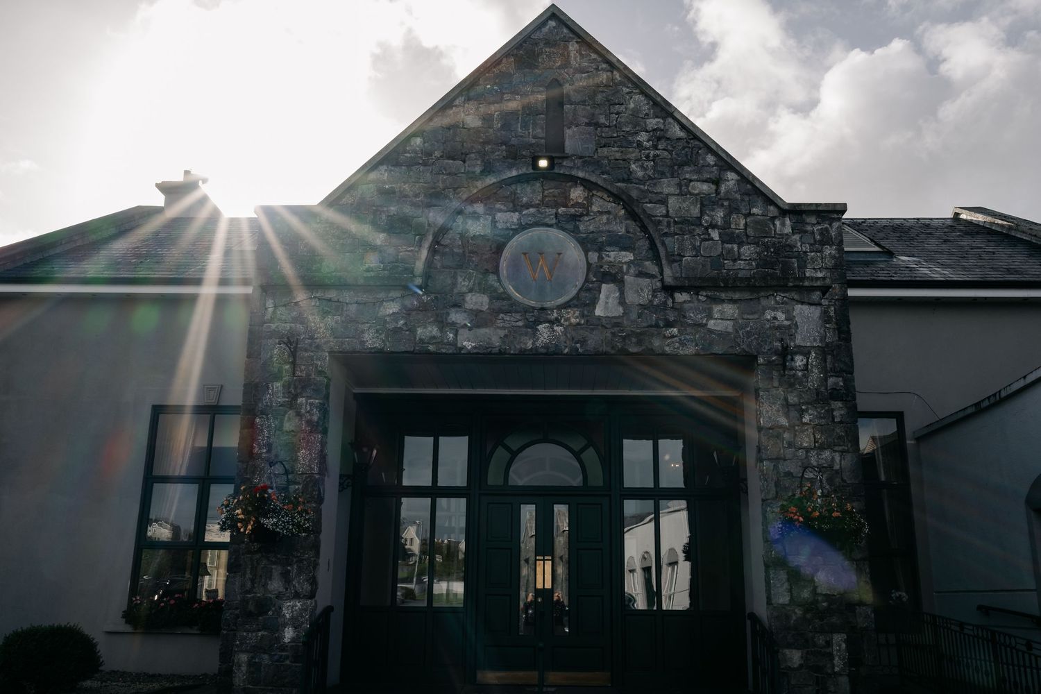Stone church exterior with sunburst peeking through clouds above the entrance.