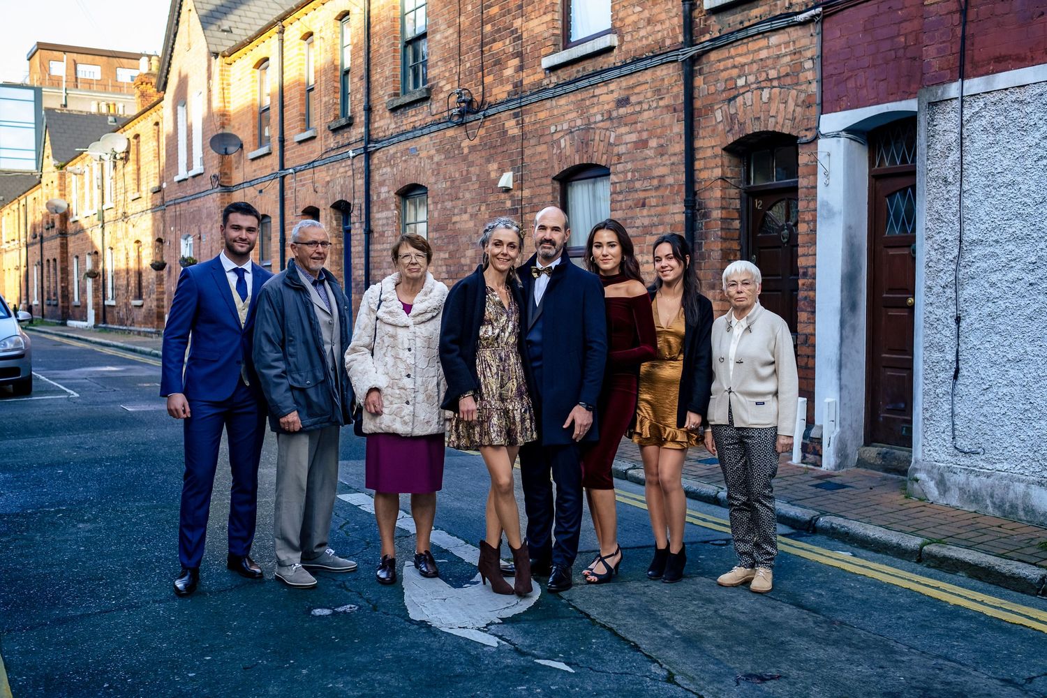 Group of eight people posing together on a street in front of red brick buildings.