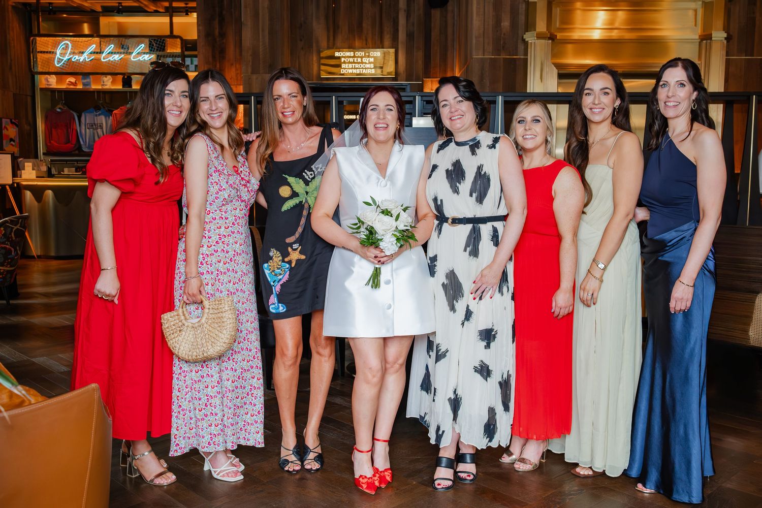 Celebration group photo at indoor venue with formal dresses in red, navy and patterned styles.