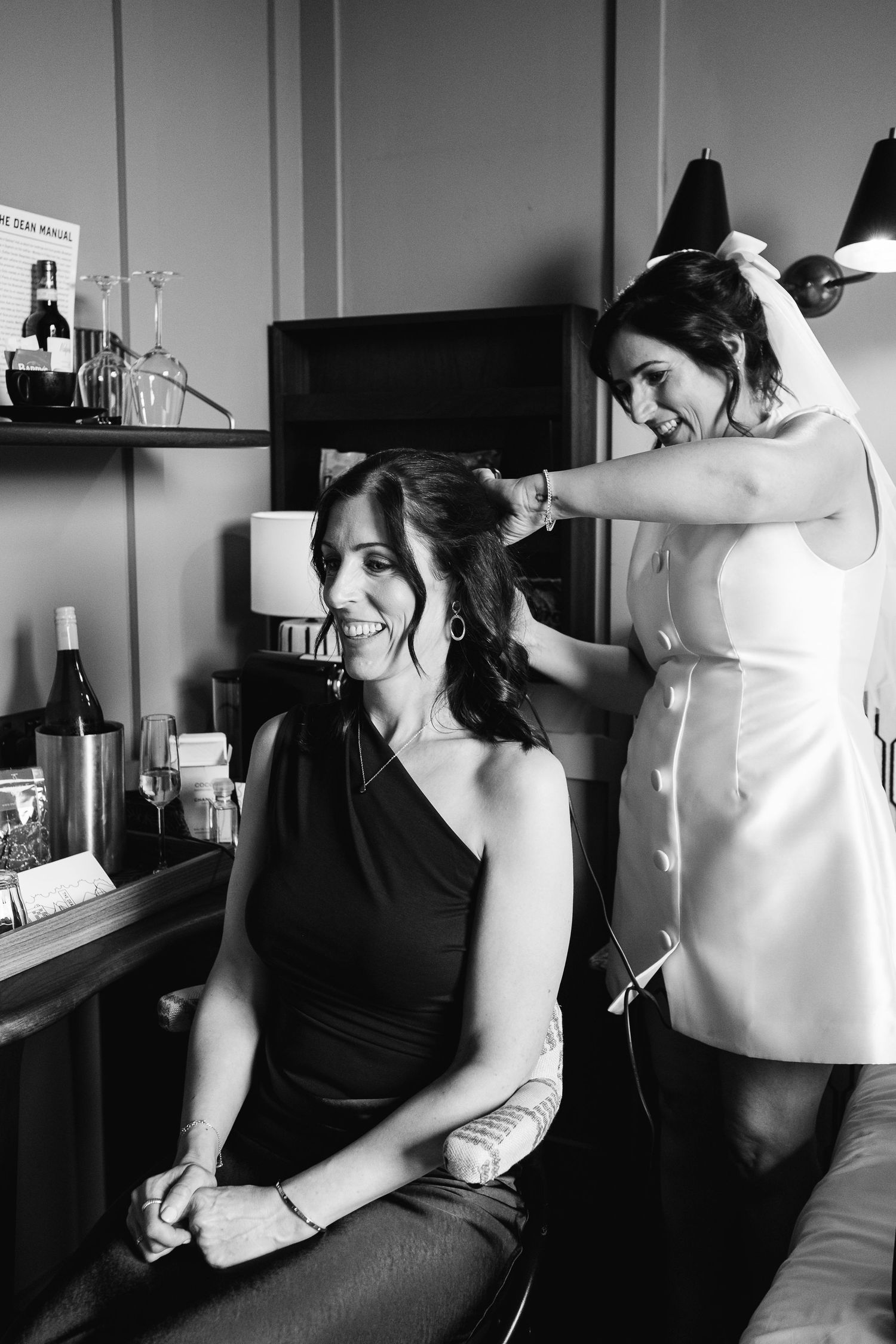 Black and white photo showing getting ready preparations with someone helping zip up a white dress.