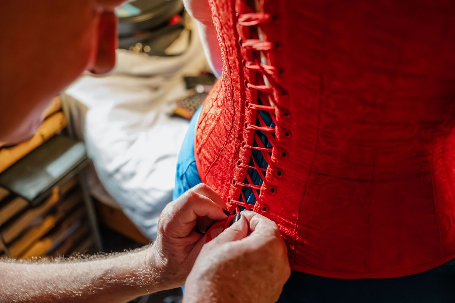 Close-up of hands lacing up a bright red corset or bodice.