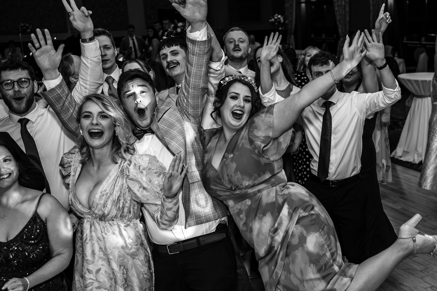 Energetic crowd of people dancing and raising hands on a dance floor at a wedding party celebration.