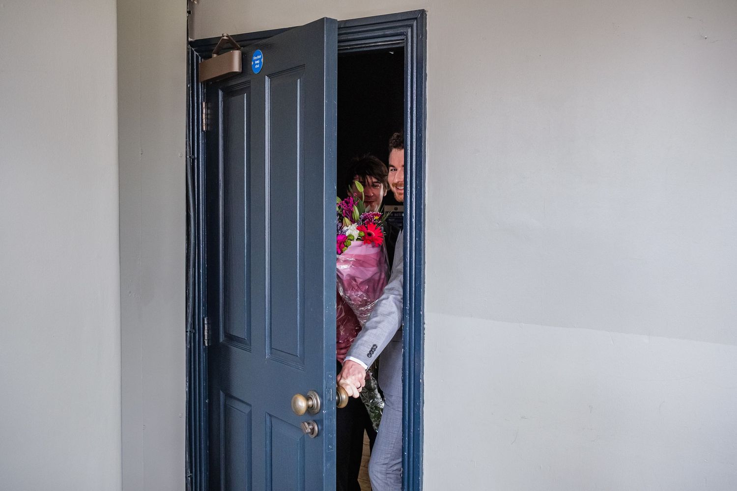 Someone peeks playfully through a dark blue doorway in a white hallway.