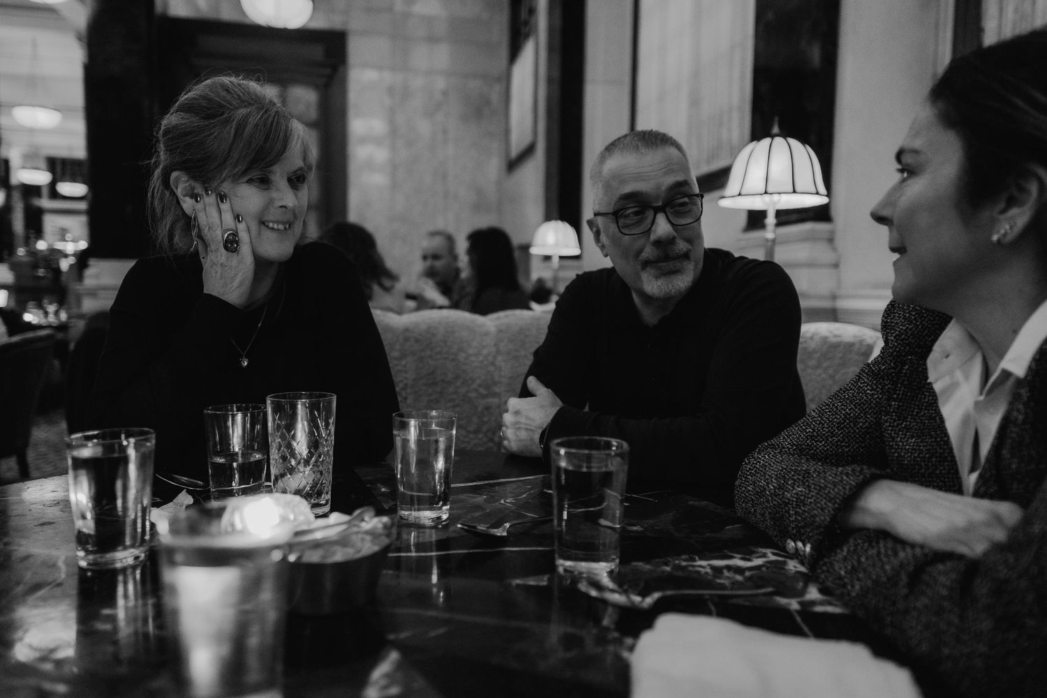 Three people engaged in conversation at a dimly lit restaurant table with drinks.