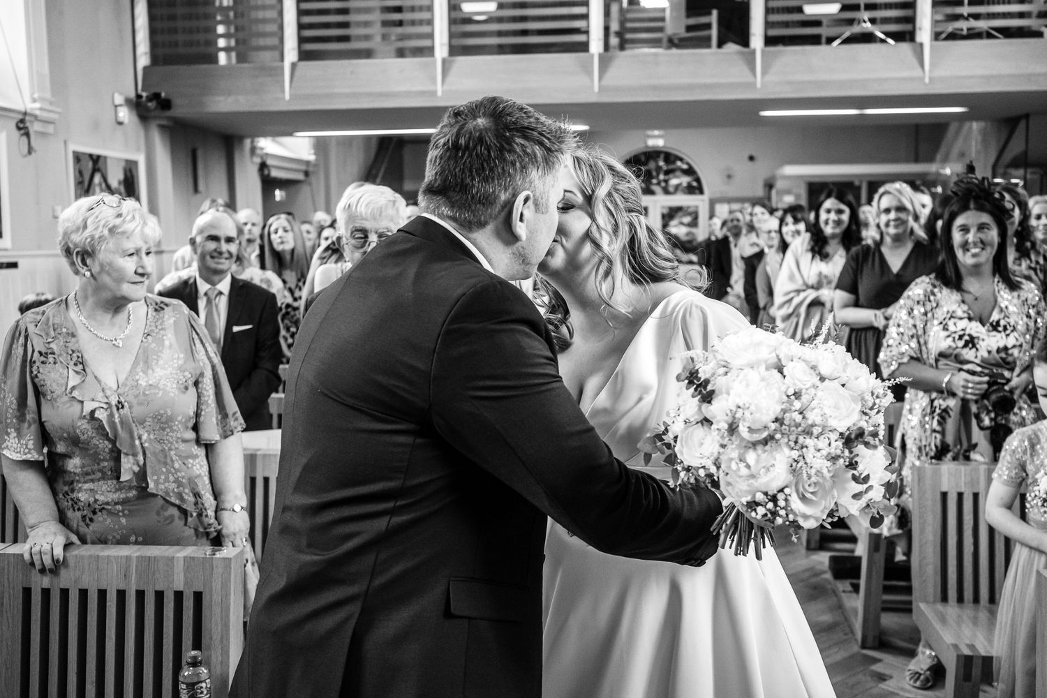 A touching moment captured during a wedding ceremony in black and white as guests look on.