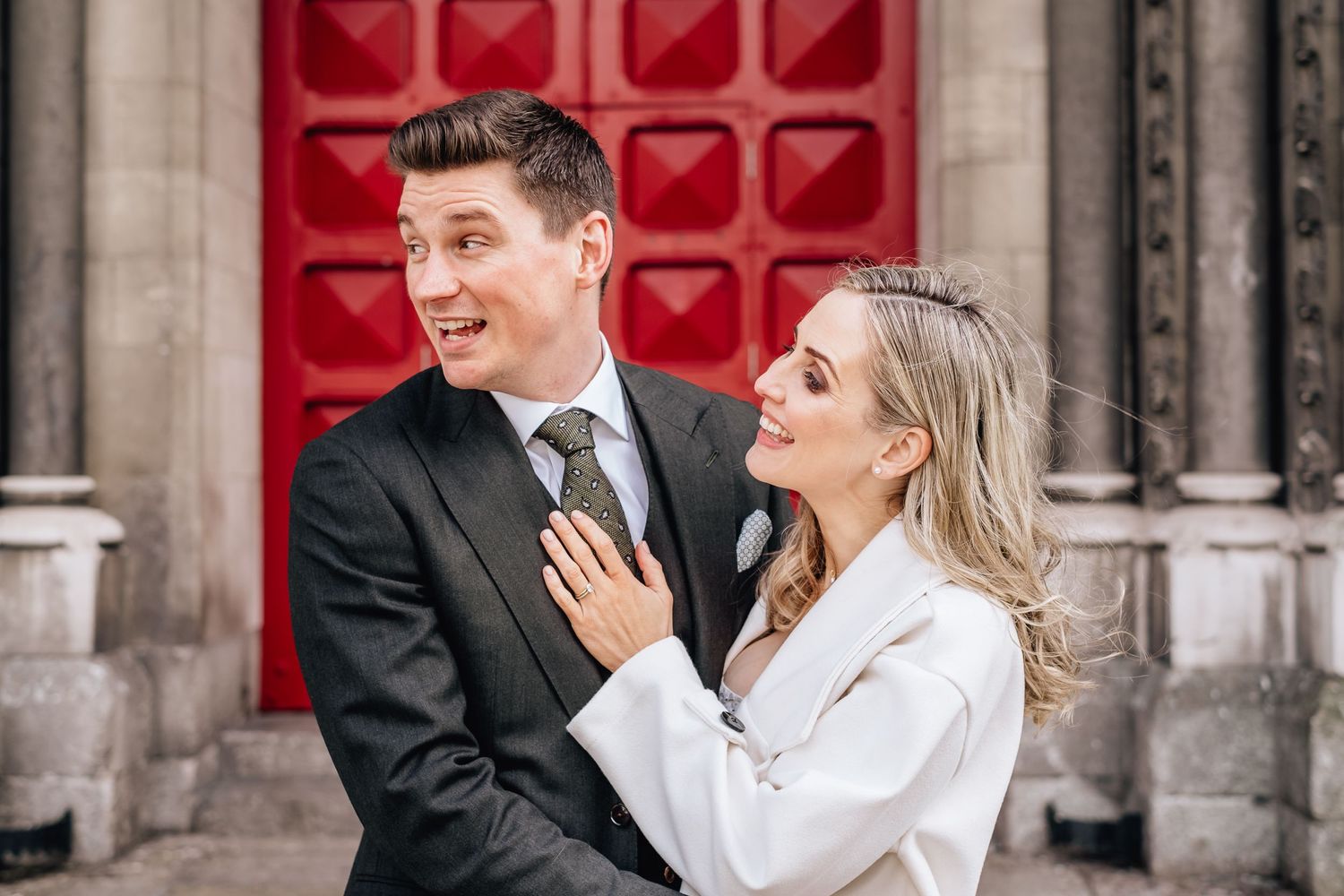 Romantic couple embraces in formal attire against vintage architectural backdrop with red door.