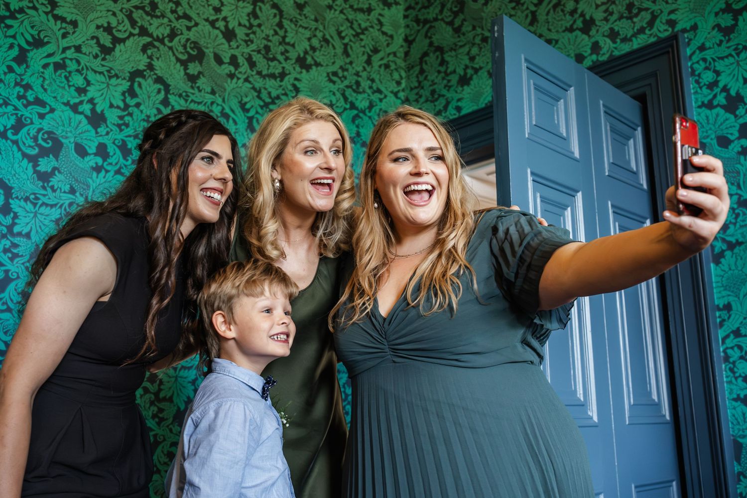 Three people taking a selfie together against a blue door and green wallpapered background.