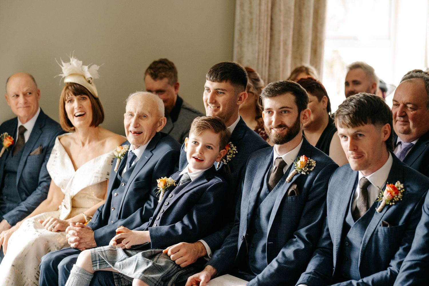 Wedding ceremony attendees seated in rows wearing formal navy suits and attire.