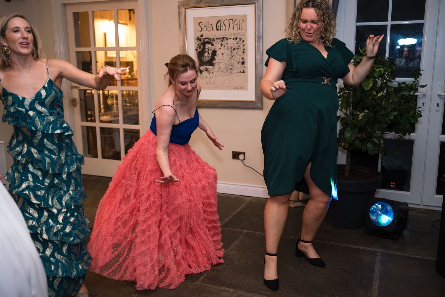 Three women in elegant dresses dancing joyfully at a formal party event.