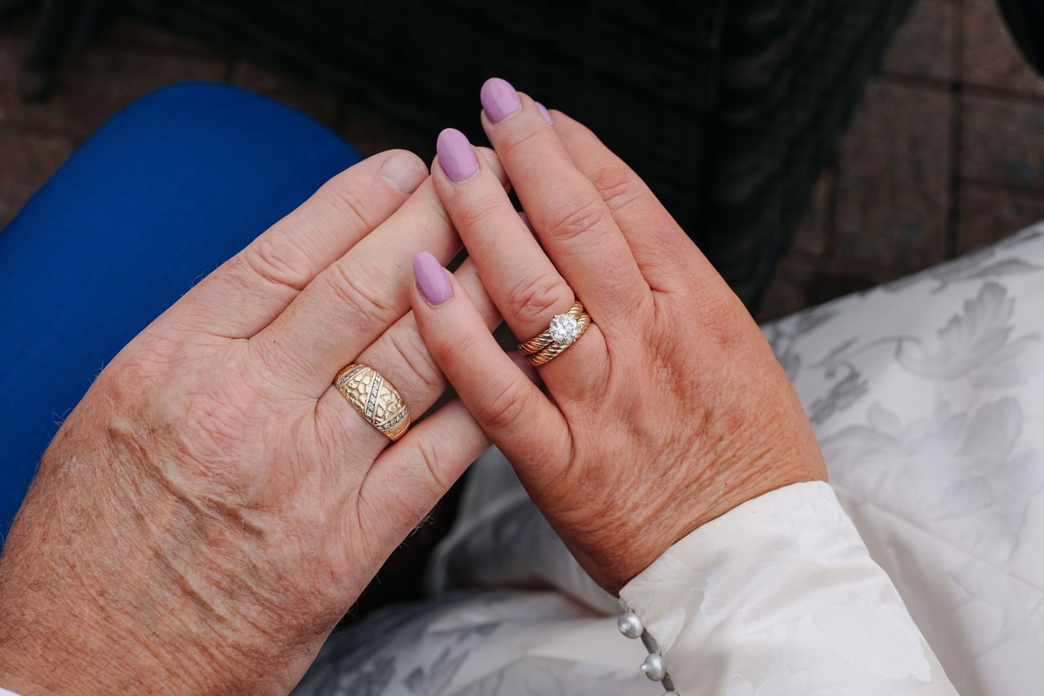 Close-up of bride and grooms hands showing wedding rings with purple manicured nails.