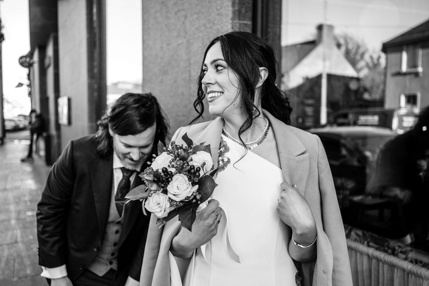 Bride smiling holding bouquet in black and white wedding photo outdoors.