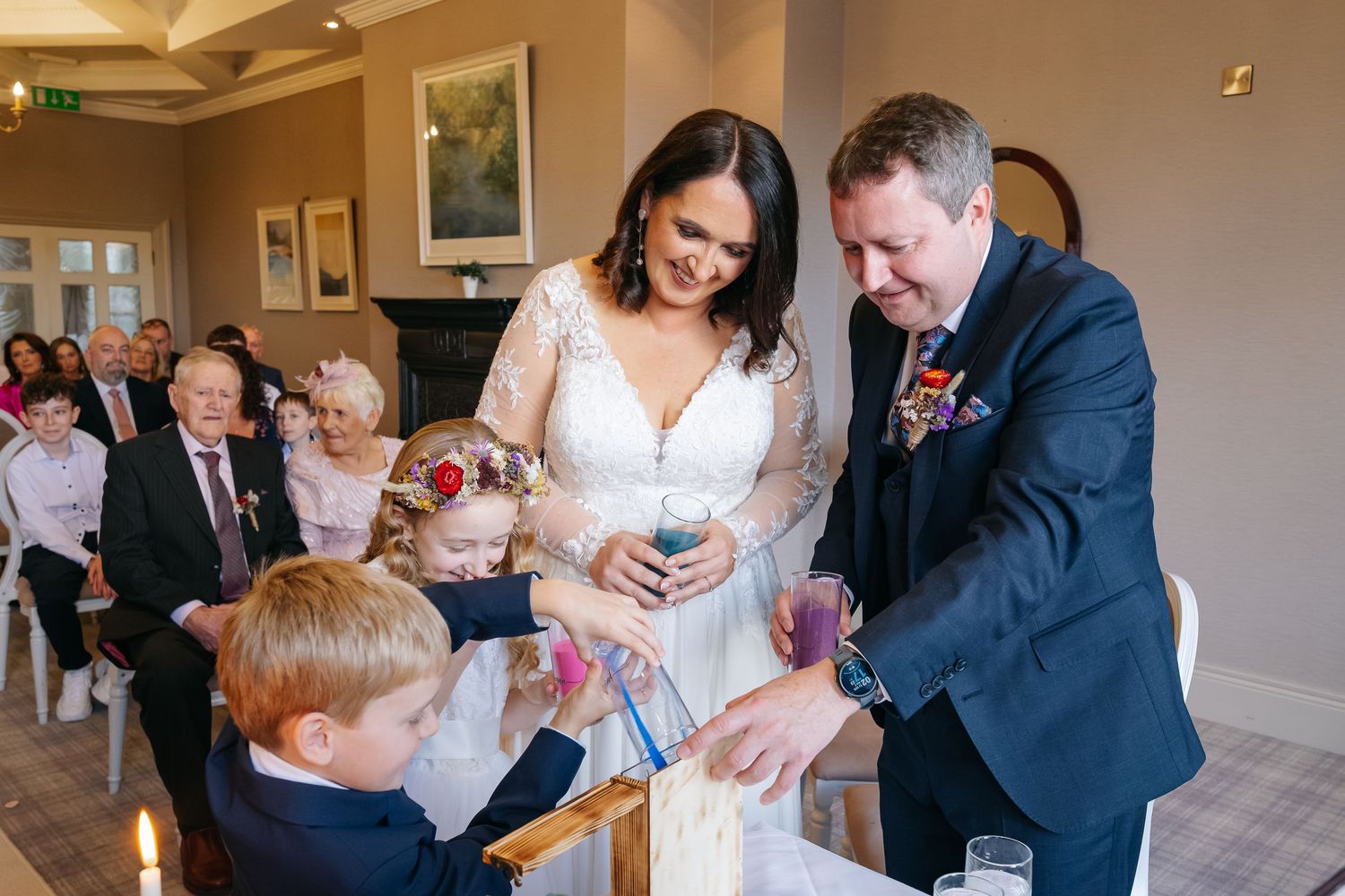 Bride and groom perform a unity candle ceremony with two children during an elegant wedding reception.