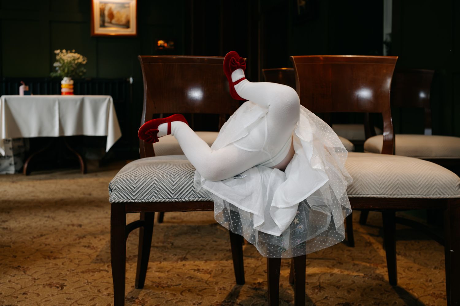 A white costume figure in a bridal dress slumped over restaurant chairs with red shoes visible.