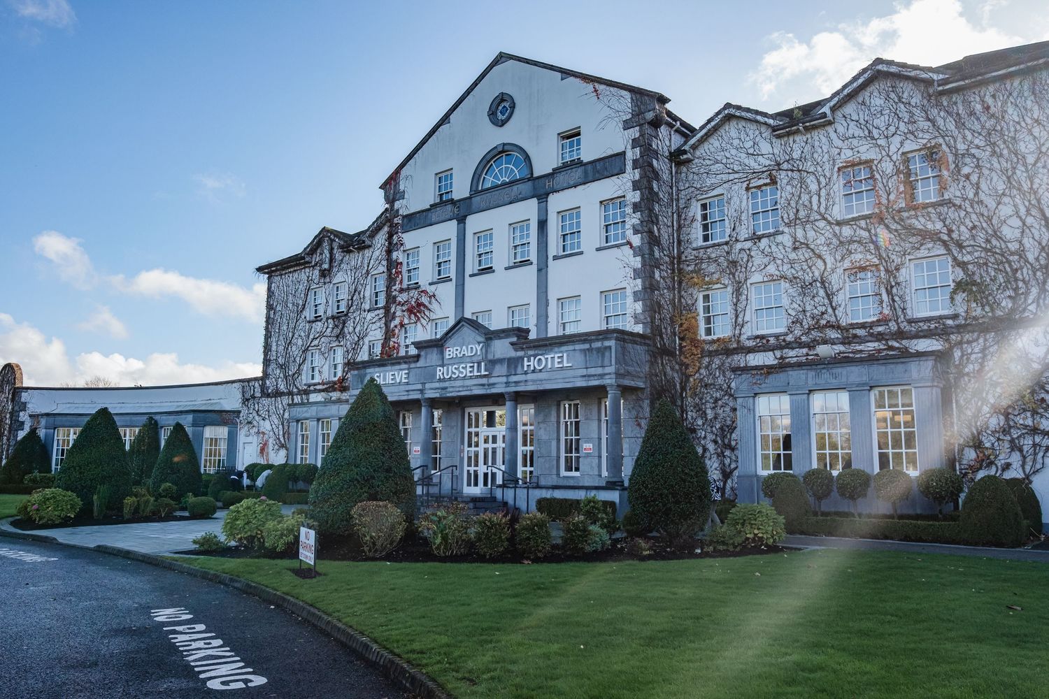 Grand Georgian hotel with ivy-covered facade, manicured gardens, and sweeping driveway on a sunny winter day.