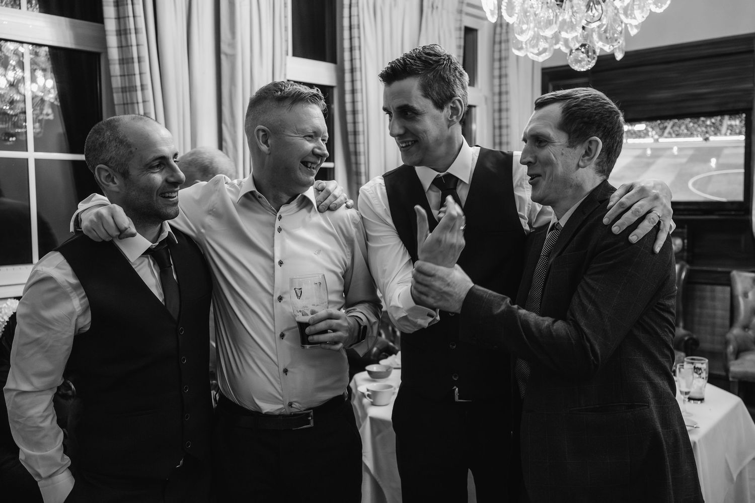 Four groomsmen laughing and celebrating together in black and white wedding reception photo.