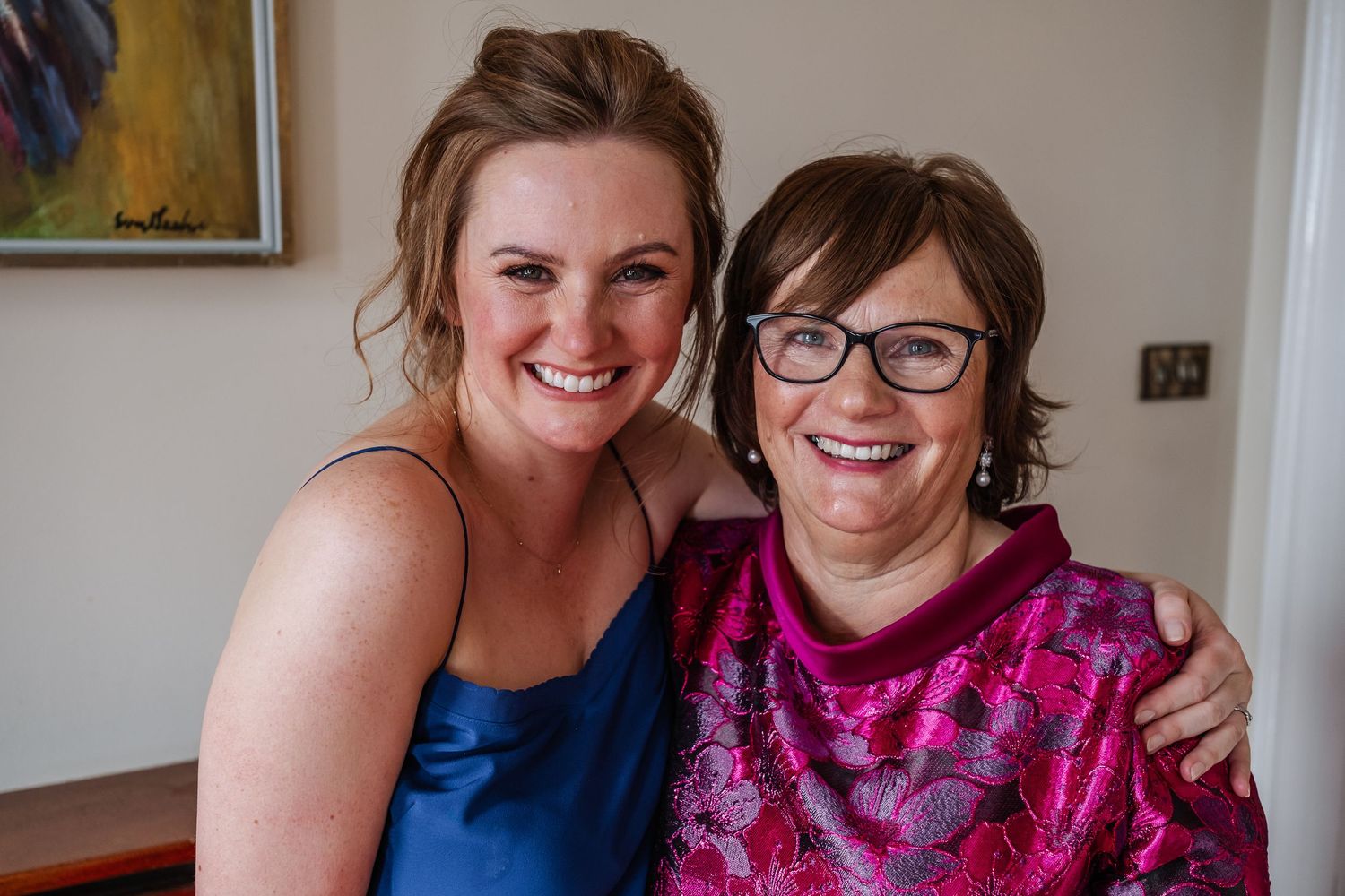 Two smiling women pose together, one in a blue dress and one in a pink floral top, at a formal event.