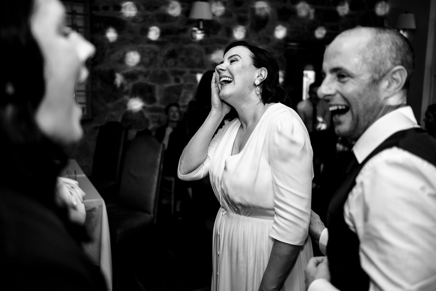 Bride laughing with guests during wedding reception in black and white photo.