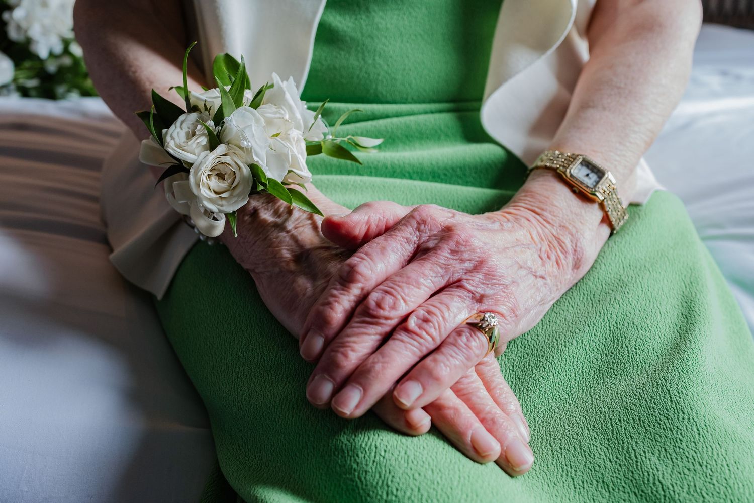 Close up of hands wearing corsage against green dress fabric.