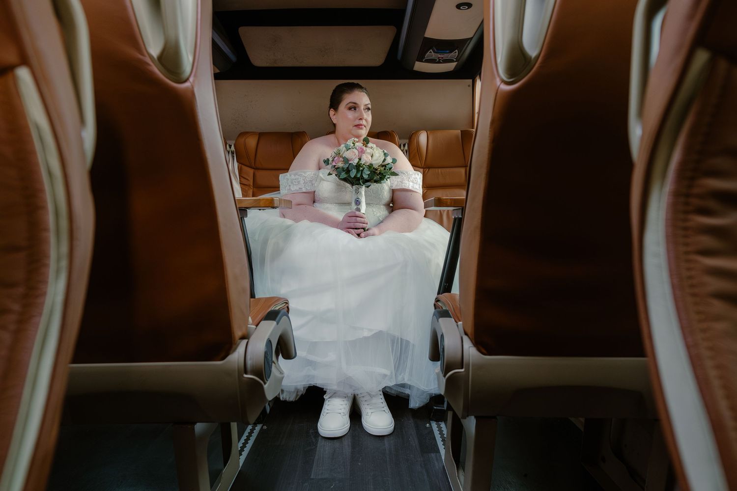 Wedding photo of person in white dress sitting in vintage vehicle with bouquet.