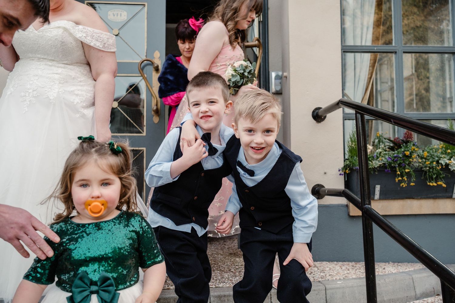Children in formal attire play and pose on outdoor steps during a celebration.