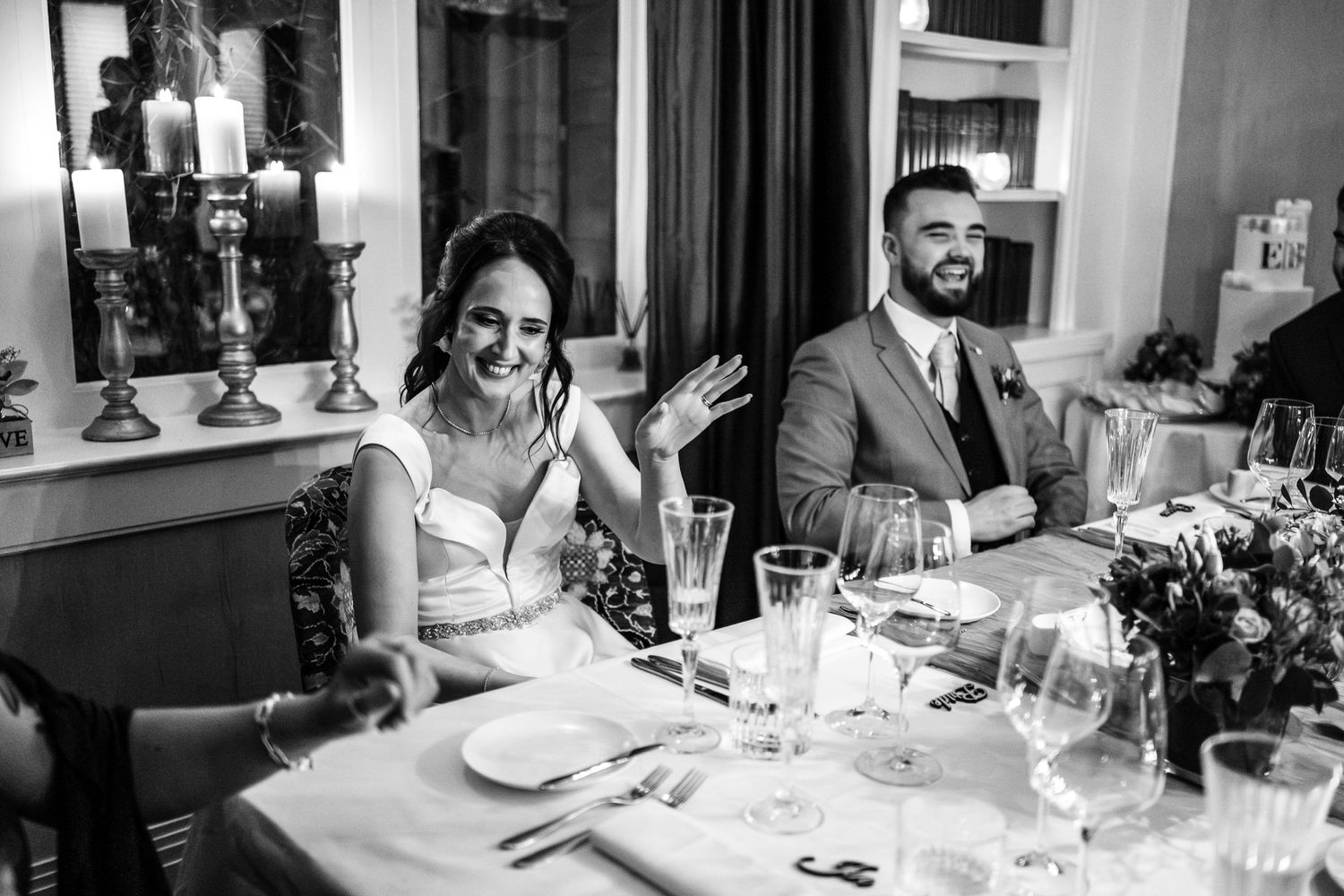 A black and white photo of newlyweds enjoying their reception dinner at an elegant table setting.