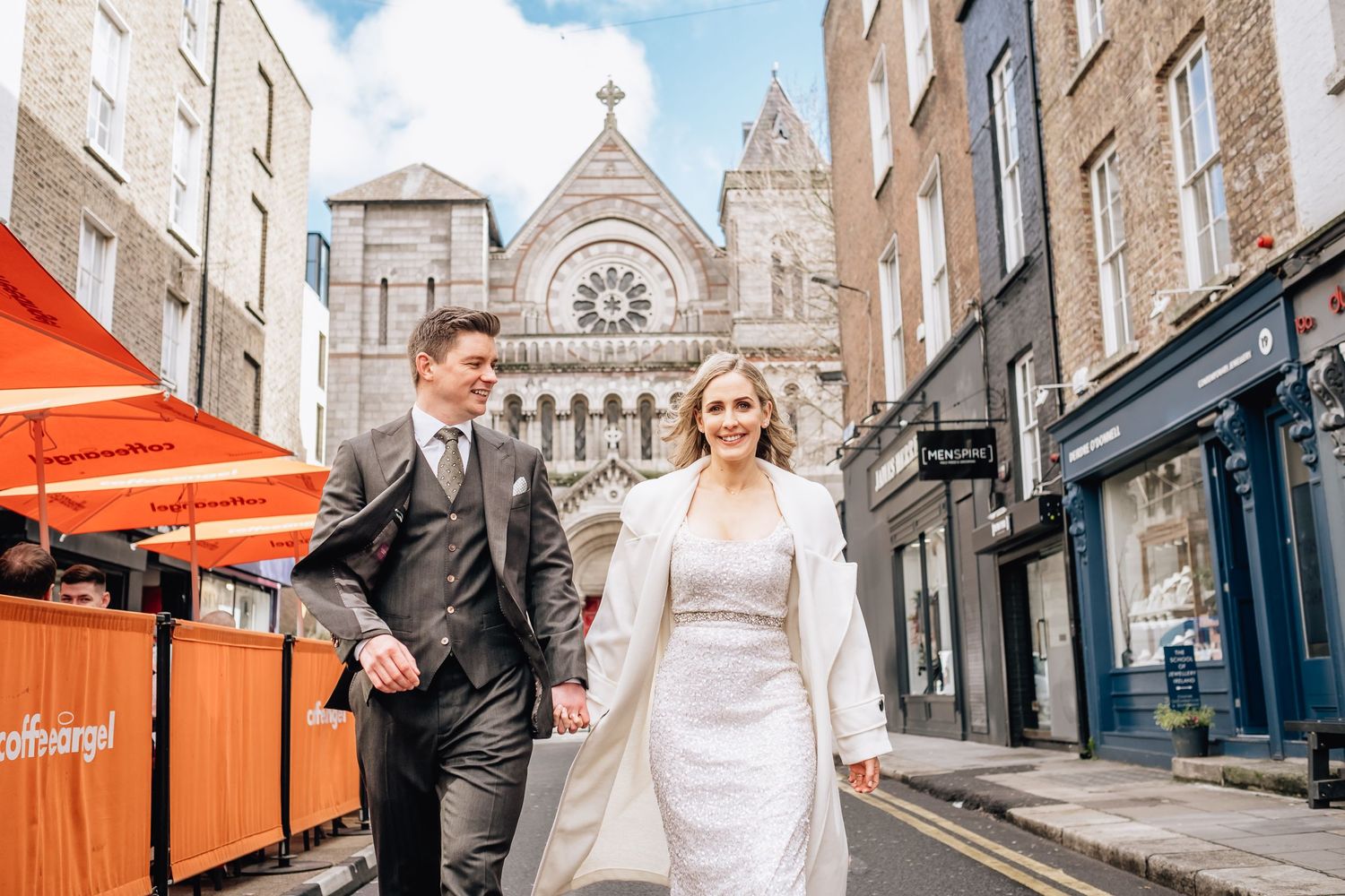 Couple walks hand in hand past historic church with orange barriers visible.