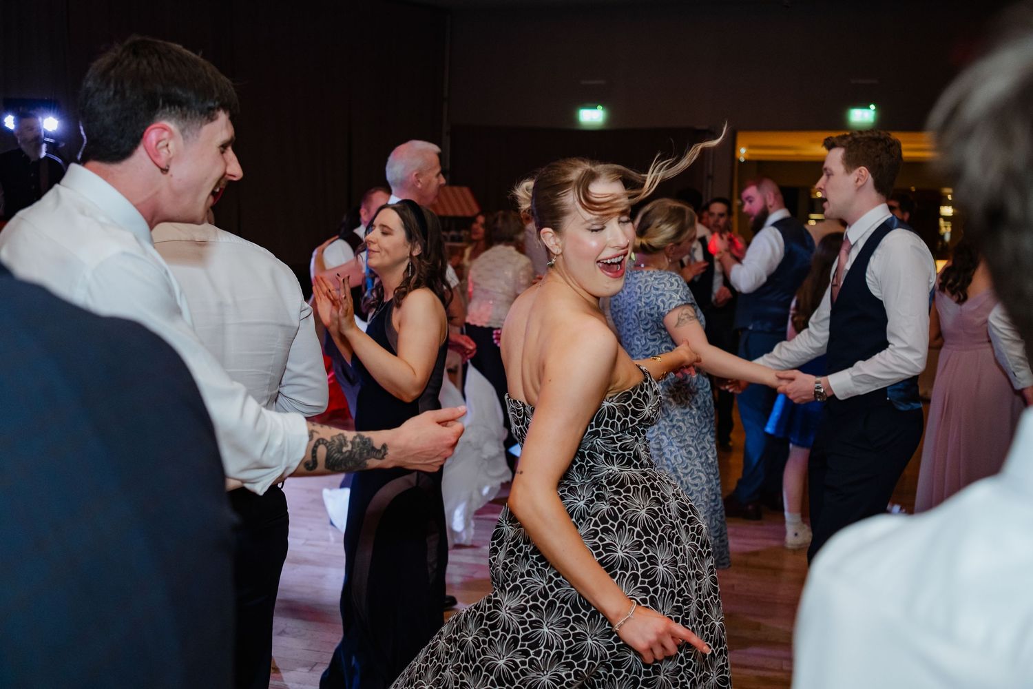 Wedding guests dance and enjoy themselves on a lively dance floor during an evening reception celebration.