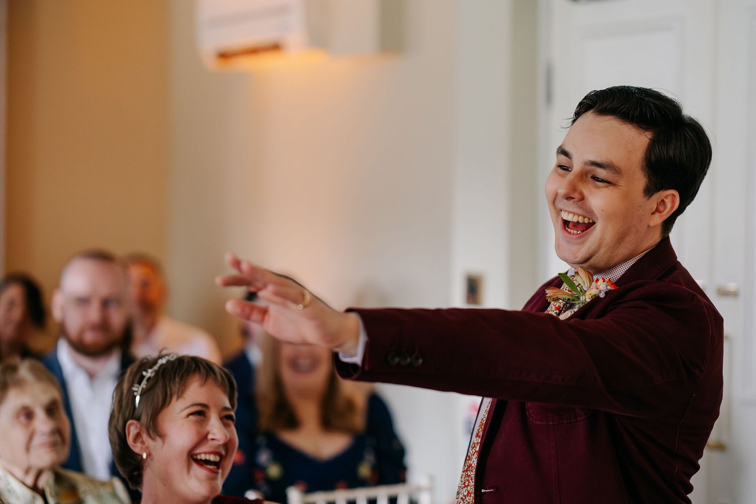 Wedding guests laugh and celebrate during a reception in burgundy attire.